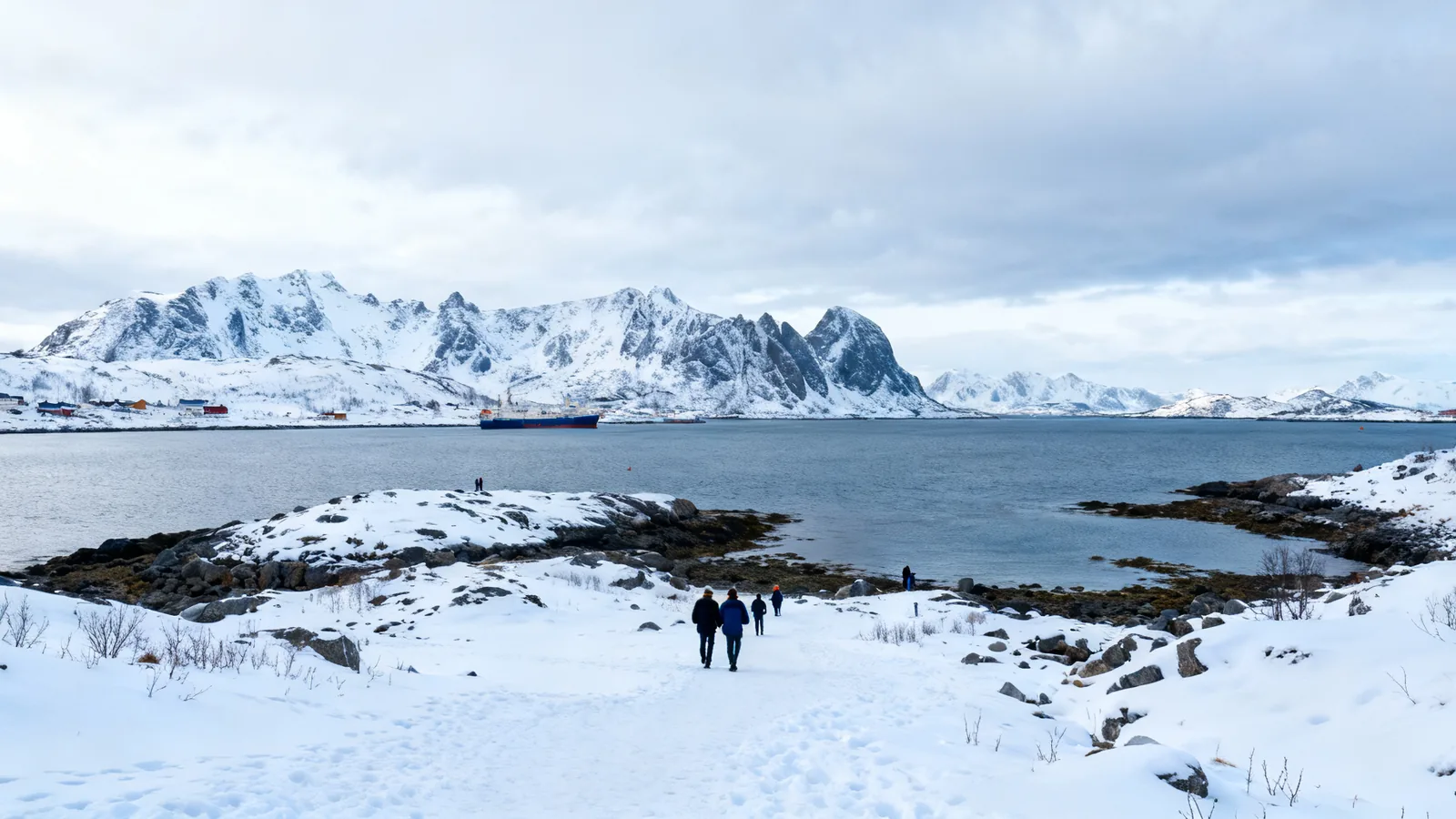 Distant walkers on a snowy shoreline beneath mountains