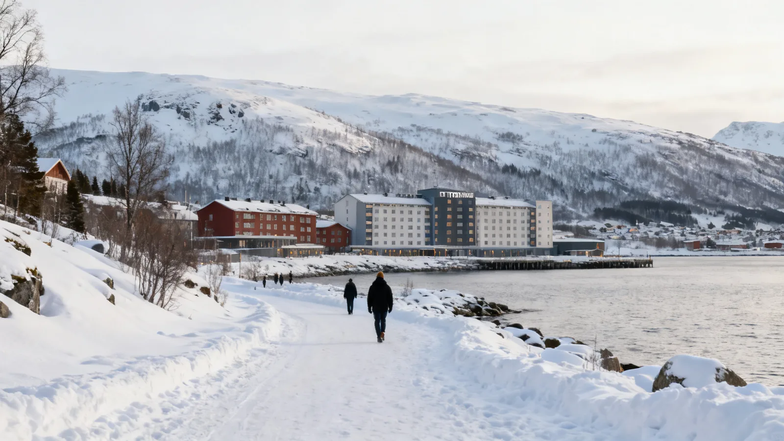Walkers beside a snowy coast and waterfront buildings